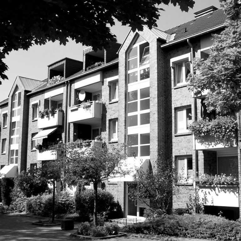 Außenfassade einer Wohnanlage in Dortmund. Mehrstöckiges Wohngebäude mit Balkonen und Bäumen im Vordergrund.