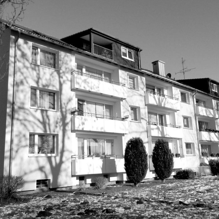 Balkone und Garten eines Mehrfamilienhauses. Mehrstöckiges Wohngebäude mit Balkon und Schatten von Bäumen im Vordergrund.