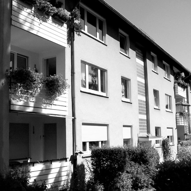 Hauseingang und Fassade eines Wohnhauses. Mehrfamilienhaus mit Balkonen und Pflanzen, schwarz-weiß.