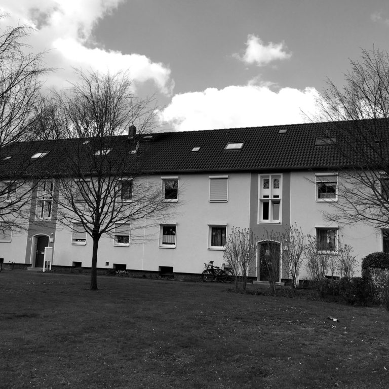 Hauseingang in Selm. Mehrstöckiges Wohngebäude mit Bäumen und einem Rasenbereich im Vordergrund.