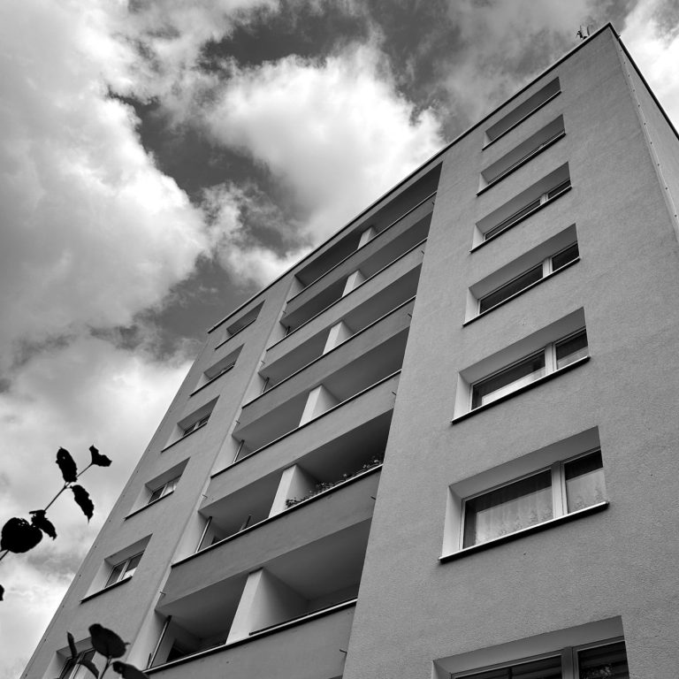 Balkon eines Hochauses in Lage. Hochhaus mit grauer Fassade und wolkigem Himmel im Hintergrund.